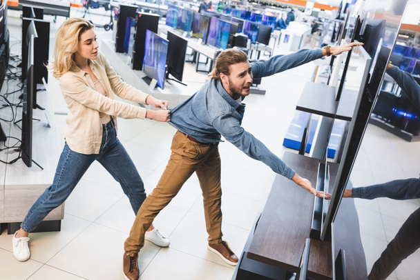 girlfriend pulling sad boyfriend with tv in home appliance store  - Photo, Image