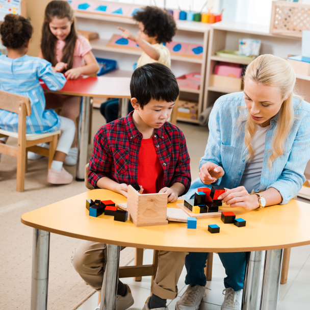 Montessori okulunda çocuklarla inşaat blokları oynayan öğretmen ve çocuğun seçici odak noktası   - Fotoğraf, Görsel