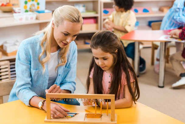 Concentration sélective d'un enfant et d'un enseignant jouant à un jeu en bois avec des enfants en arrière-plan à l'école montessori
 - Photo, image