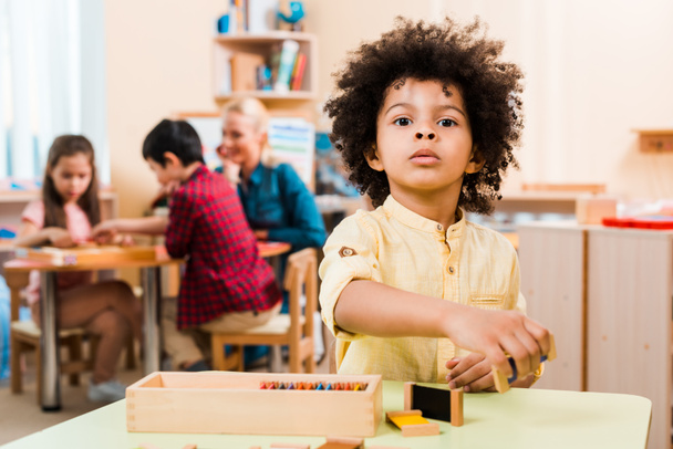 selektiver Fokus eines afrikanisch-amerikanischen Kindes mit Holzspiel und Lehrer mit Kindern in der Montessori-Schule - Foto, Bild