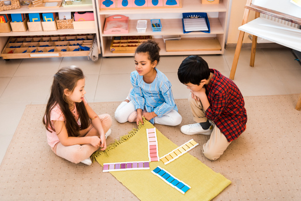 Montessori sınıfında yerde oturmuş oyun oynayan çocukların yüksek açılı görüntüsü - Fotoğraf, Görsel