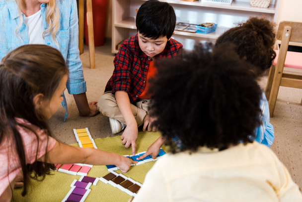 Selective focus of kids folding colorful game by teacher on floor in montessori school  - Foto, Imagen