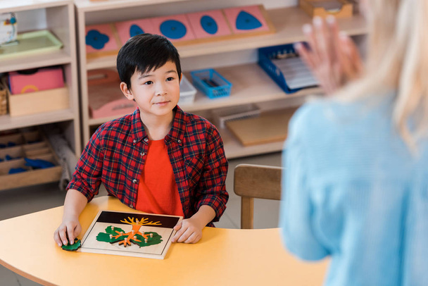Asyalı çocuğun Montessori okulunda öğretmenine bakışının seçici odak noktası. - Fotoğraf, Görsel