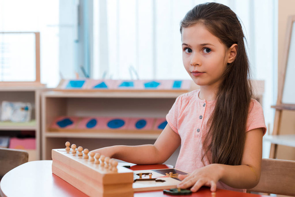 Child folding educational game and looking at camera at desk in montessori school - Photo, Image