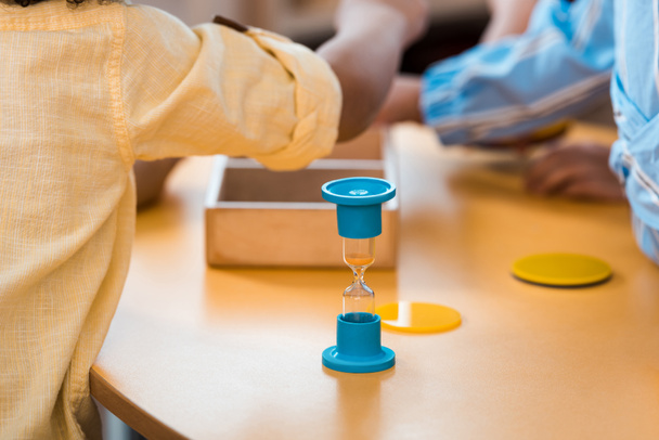 Enfoque selectivo de los niños con juego educativo y reloj de arena en el escritorio en la escuela montessori
 - Foto, Imagen