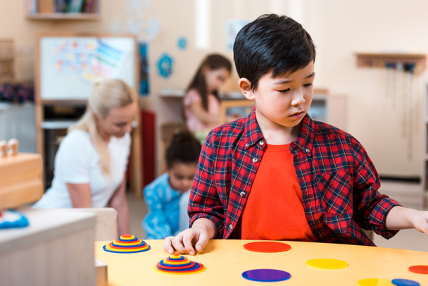 Selektywne skupienie azjatyckiego dziecka składanie gry i nauczyciel z dziećmi w tle w szkole montessori - Zdjęcie, obraz