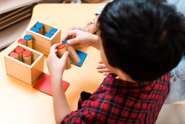 モンテッソーリ学校の机で木製ゲームをプレイする子供と教師の選択的な焦点、オーバーヘッドビュー - 写真・画像