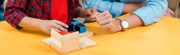Vista recortada del maestro y el niño jugando bloques de construcción en el escritorio en la clase montessori, plano panorámico
  - Foto, Imagen