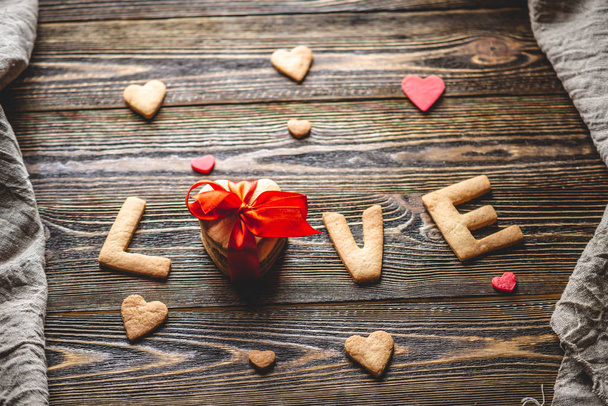 Boodschap van een zoet koekje in de vorm van het woord liefde en een geschenk gebonden met rood lint. Romantisch Valentijnscadeau - Foto, afbeelding