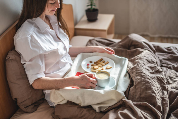 Woman have a romantic Breakfast in cozy morning bed. Coffee and word love from cookies. Surprise on Valentine's day - Valokuva, kuva