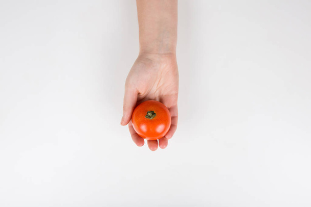 Κοντινό πλάνο ενός ανθρώπινου χεριού που κρατά μια φρέσκια κόκκινη ντομάτα απομονωμένη στις  - Φωτογραφία, εικόνα