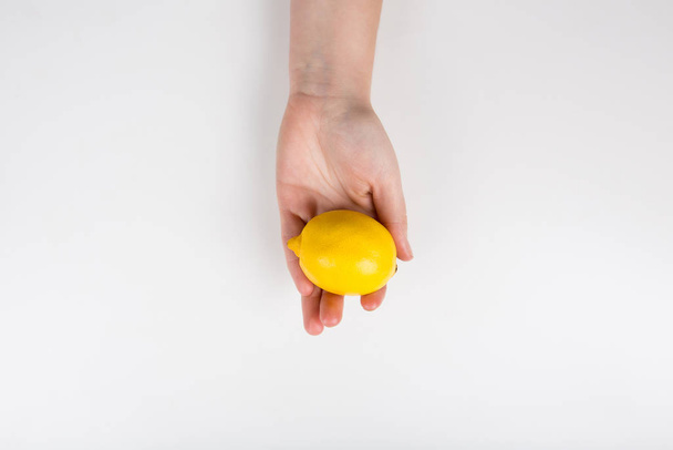 Nahaufnahme einer menschlichen Hand, die eine frische gelbe Zitrone hält  - Foto, Bild