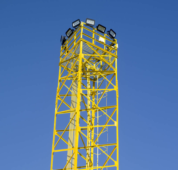 Желтая металлическая башня со многими свинцовыми лампами в небе
 - Фото, изображение