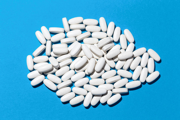 Ovale witte supplementen van calciummagnesium op blauwe papieren achtergrond. - Foto, afbeelding