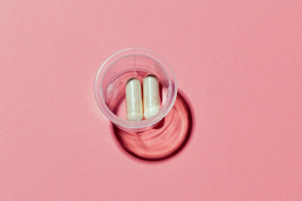 Tappo di misura in plastica con pillole mediche su sfondo rosa. - Foto, immagini