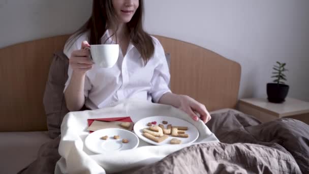 Young woman have a romantic Breakfast in morning bed. Coffee and word love from cookies. Surprise on Valentines day - Záběry, video