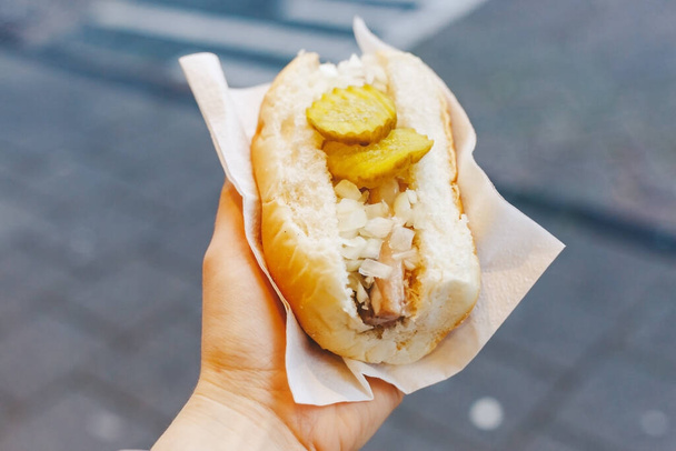 Holland herring fish in female hand outside. Traditional Dutch street food, herring fish. Stock photo street food, herring fish in a bun with onions and pickles. - Foto, immagini