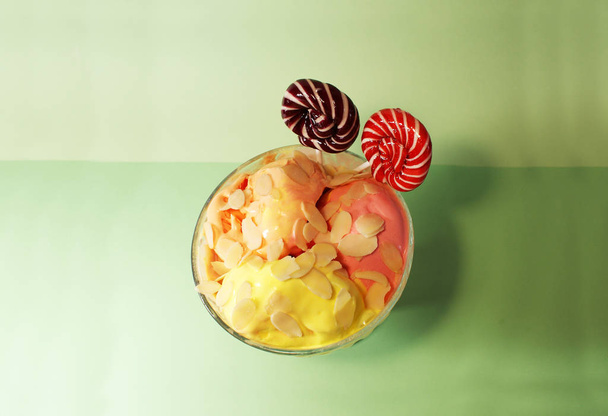 Fruit ice cream with nuts, candies on a colored background. - 写真・画像