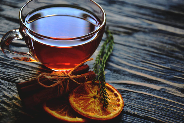 Kopje thee, gedroogde plakjes sinaasappel en kaneelstokjes op een donkere houten ondergrond. Close-up. - Foto, afbeelding