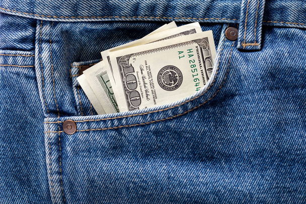 US dollar banknotes in the front left pocket of blue jeans. Concept of saving money or pocket expenses - Photo, Image