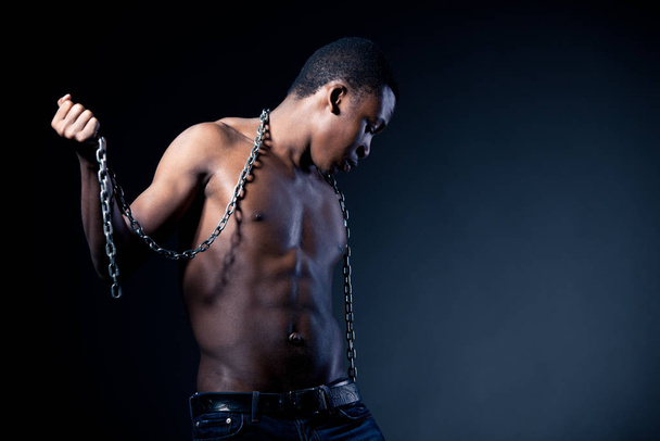 Young half naked african man standing and holding massive chains in hands - Photo, image