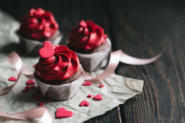 濃い木製のテーブルの上に甘い心で飾られた赤い色のバレンタインカップケーキ. - 写真・画像
