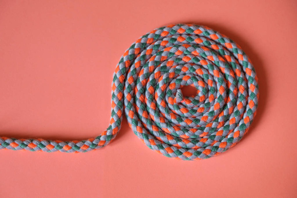 Kordel-Spirale an einem Rand rosa Oberfläche. Kordel aus drei Farben rosa, grün, grau. Kopierraum. - Foto, Bild
