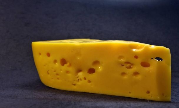 Koyu bir arkaplanda delikleri olan bir dilim peynir. - Fotoğraf, Görsel