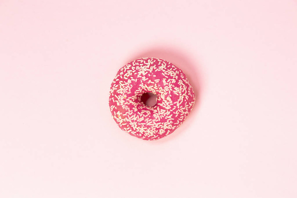 ein Donut in rosa Glasur mit weißen Streuungen auf rosa Hintergrund. Süßigkeiten und Desserts. minimalistischer Hintergrund mit sauberem Platz für die Inschrift. Kopierraum. - Foto, Bild
