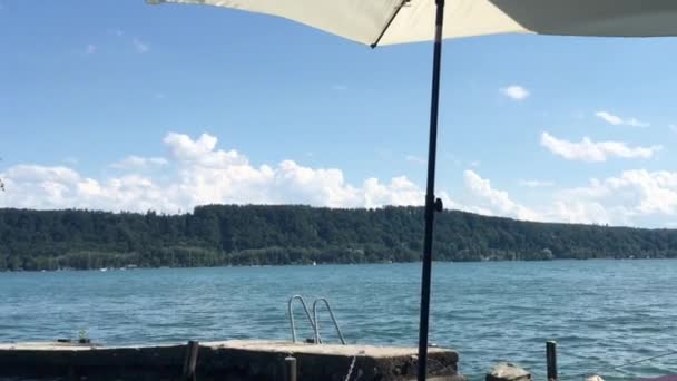 Klidná scéna se slunečníkem v mírném větru za slunečného dne na břehu jezera Bieler See. - Záběry, video