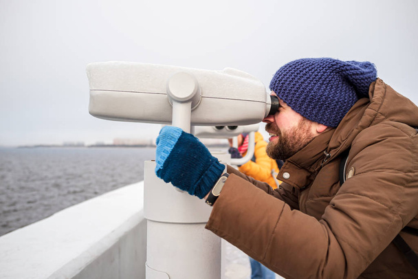 Man looks with interest in the tower viewer, standing on the promenade, on a blurred background of the sea and the city. - Photo, Image