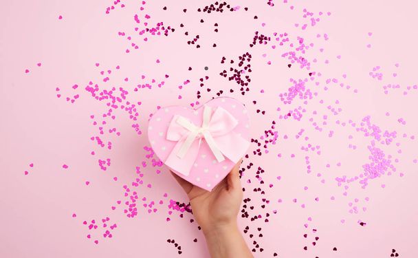 mano femenina sosteniendo una caja de cartón rosa con un lazo en una ba rosa
 - Foto, Imagen
