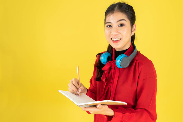 fiatal hölgy piros ingben ír egy könyvet sárga háttér - Fotó, kép