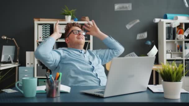 Entrepreneur relaxing in chair in office while money banknotes falling from above - Materiaali, video