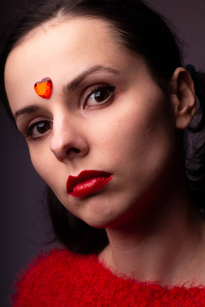dziewczyna w czerwonym swetrze z czerwonymi ustami i czerwonym sercem na twarzy - Zdjęcie, obraz