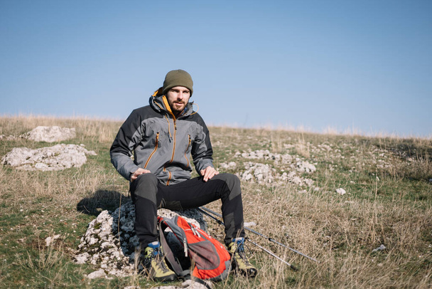 Bearded hiker with hiking equipment resting on a stone - Photo, Image