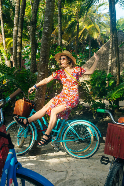 hermosa chica en un sombrero y un vestido brillante en una bicicleta en la selva - Foto, Imagen
