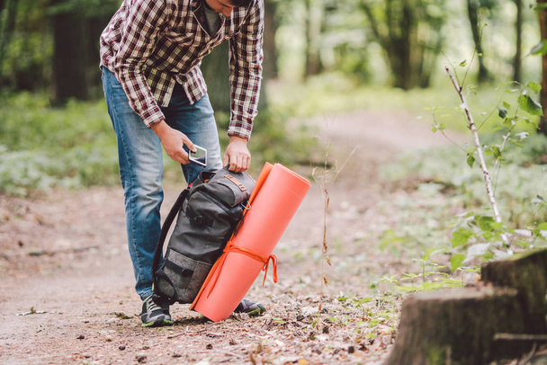 Hiker holding his camping backpack. traveler opening backpack while traveling in beautiful wood. Theme hiking and travel. Man traveling in forest with backpack. Active healthy man hiking in forest - 写真・画像