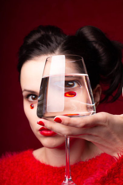 emotional girl in red  holds a glass of water in her hands - Foto, Imagen