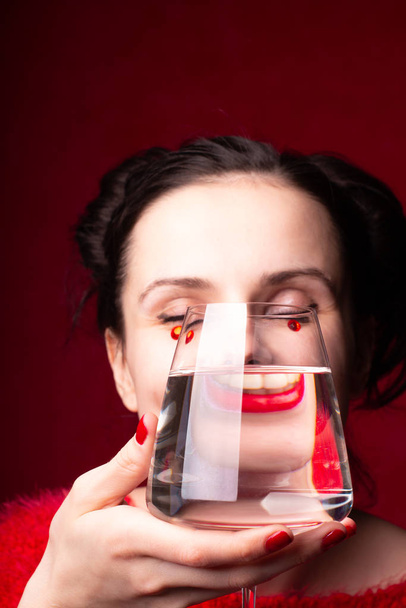 emotional girl in red  holds a glass of water in her hands - Foto, Bild