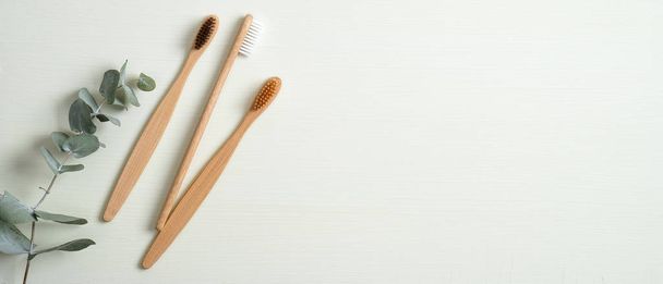 Eco-friendly bamboo toothbrushes and eucalyptus leaf on green background. Natural organic bathroom beauty product concept. Flat lay, top view, copy space - Фото, изображение