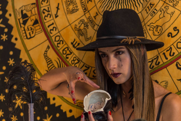 Beautiful young woman, esoteric oracle, showing a black skull with runes inside - Foto, Imagen