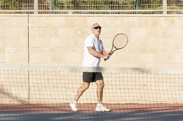 Homme âgé jouant au tennis sur un court extérieur
 - Photo, image