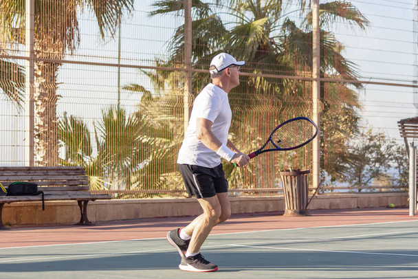 Un anciano juega al tenis en una cancha al aire libre - Foto, imagen