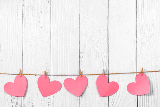 White painted wooden background with a garland of pink hearts. Natural rope and clothespins. Concept of recognition of love, romantic relationships, Valentines day in grunge style. Copy space - Zdjęcie, obraz