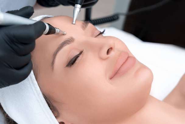 Cosmetology. Beautiful Woman At Spa Clinic Receiving Stimulating Electric Facial Treatment From Therapist. Closeup Of Young Female Face During Microcurrent Therapy - Photo, Image