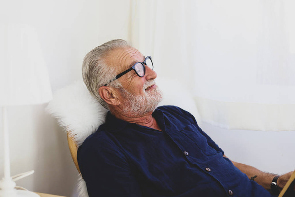 Senior man zit alleen voor ontspanning en glimlach portret in huis. - Foto, afbeelding