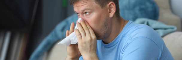 Man blowing his nose in a napkin while sitting - Photo, image