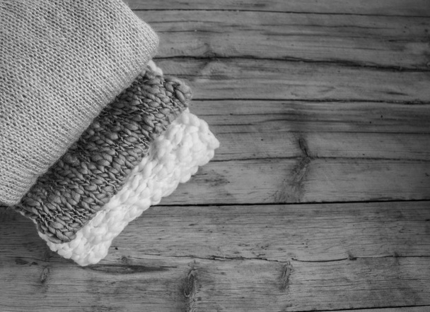 knitted things stacked in a pile lie on a wooden table. black and white photo - 写真・画像