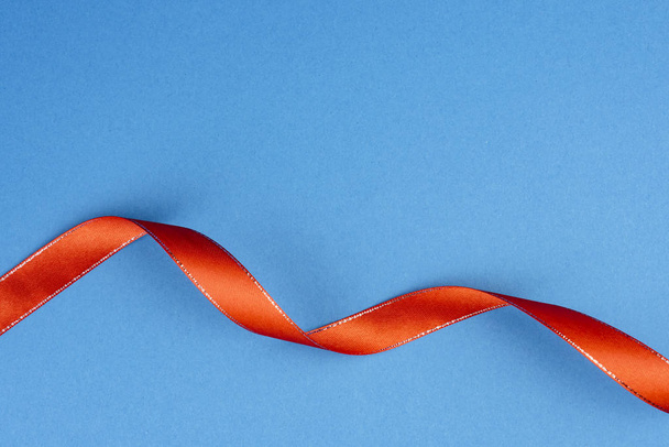Red wriggling ribbon with silver stitching on a blue background. - Foto, Bild